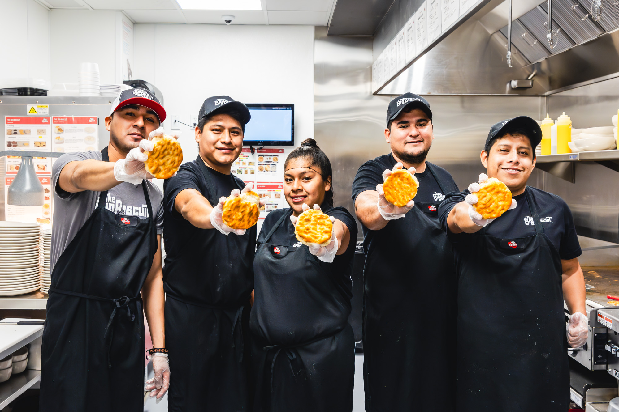 Group of people standing in a restaurant kitchen and holding biscuits to the camera