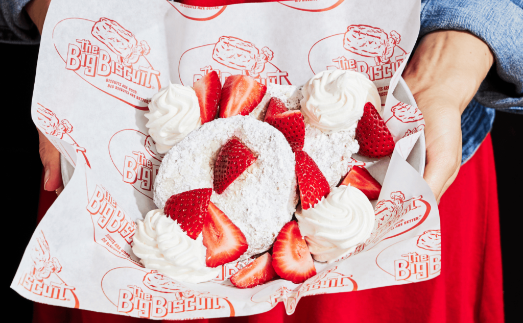 Hands holding tray for bonuts, strawberries, whipped cream