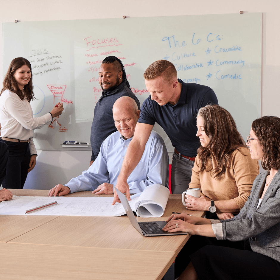 Group of people standing and sitting around table, looking at paperwork